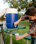 Child using 2 Gallon Portable Sports Cooler Water Beverage Dispenser Insulated Cooler With Spigot And Swing Up Handle on picnic table.