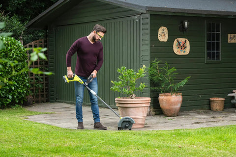 Person using 18V ONE Plus Cordless Edger Bare Tool With 22cm Serrated Edging Blade, Four Position Height Adjustment, Dual Guide Wheels, Debris Guard on lawn.