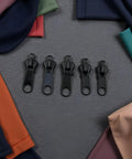 Six Black Zipper Sliders Replacement Kit For Quick Fixes On Jackets Backpacks And Clothes Instant Zip Repair Pack With Universal Fit And Easy No Sew Upgrades Grab And Go displayed with colorful fabric background.