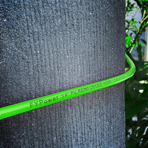 Built Like A Tank 1/4 Inch By 50 Feet Reinforced Polyurethane Air Compressor Hose coiled on textured surface.