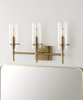 Brass Gold Modern Farmhouse LED Vanity Light Sconce With Clear Glass Cylinder Shade above mirror, three lights, wall mounted