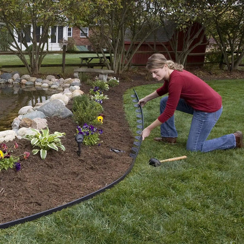 Person installing No Dig Landscape Edging System For Quick Easy Diy Lawn Borders 40 Ft Run around garden bed, using anchoring spikes.