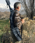 Man outdoors carrying Heavy Duty Weatherproof Long Rifle And Shotgun Slicker All Weather Rain Guard Alpine Mountain Camo Fits 38 To 56 Inch Barrels