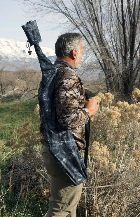 Man outdoors carrying Heavy Duty Weatherproof Long Rifle And Shotgun Slicker All Weather Rain Guard Alpine Mountain Camo Fits 38 To 56 Inch Barrels