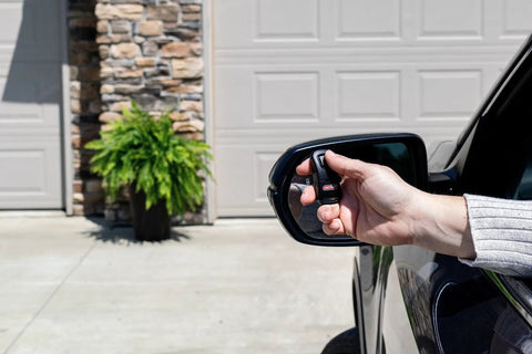 Hand holding Single Button Garage Door Opener Remote for Intellicode Compatible Openers near car mirror