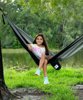 Girl sitting in Parachute Nylon Hammock Single With 2 Tree Straps by a lake, ultra portable lightweight camp gear