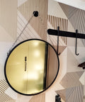 Round mirror hanging on chain against geometric patterned wall in well-lit room with hooks nearby.