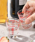 Hand holding a Two Pack Shot Glass Measuring Cup Set With Thick Base, Multi Unit Liquid Measuring Cup For Espresso And Drinks