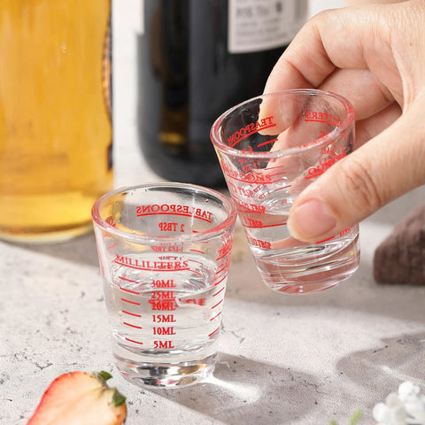 Hand holding a Two Pack Shot Glass Measuring Cup Set With Thick Base, Multi Unit Liquid Measuring Cup For Espresso And Drinks