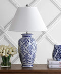 Chinoiserie Blue And White Ceramic Table Lamp With Urn Silhouette, Traditional Asian Inspired Living Room Or Bedroom Lighting, White Linen Shade, LED Bulb Included, ETL Listed For Safety on wooden table with books and flowers