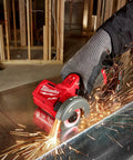Milwaukee 12V cut-off tool, red with gray guard, cutting metal as sparks fly in workshop
