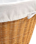 Close-up of rattan laundry basket with easy carry handles and removable white cotton liner, natural wicker texture visible.