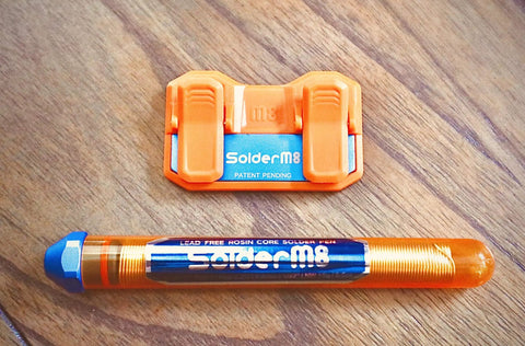 Magnetic Soldering Jig With Nano Suction Base next to orange soldering tool on wooden surface