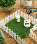 Four Piece 35 Inch Fairy Garden Wood Picket Fence Set For Dollhouse Miniature Village Landscape And DIY Diorama Projects White Color Durable Moisture Proof Great For Tiny Plant Pots And Cute Garden Scenes enclosing grass with decorations.