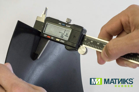 Close-up of digital caliper measuring a black MATNIKS neoprene rubber sheet (6x6 in, 1/16 in thick)