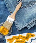 Paintbrush from 30 Piece Paint Brush Set With Thick Wooden Handles For Wood Furniture Walls Decks And Fences sits by yellow paint.