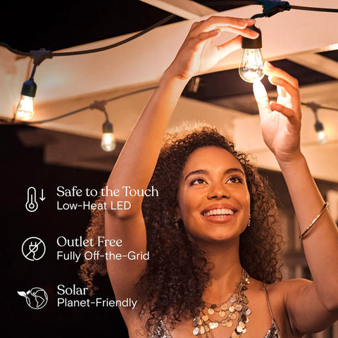 Ambience Pro 27 Ft Solar Powered Outdoor String Lights With 12 Shatterproof LED Bulbs in use on patio, woman enjoying light