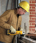 Side view of a DEWALT 20V MAX cordless 4-1/2-inch grinder in use by a construction worker wearing a yellow hard hat