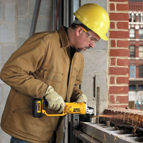 Side view of a DEWALT 20V MAX cordless 4-1/2-inch grinder in use by a construction worker wearing a yellow hard hat