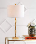 Gold Leaf 29-Inch Geometric Column LED Table Lamp With White Linen Drum Shade on glass table next to decorative vase and book