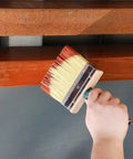 Hand using 5 inch Deck Stain Brush Set 3 Pack Featuring 4 Inch 5 Inch And 6 Inch Sizes with stainless steel ferrule on wood surface