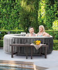 Two Pack PureSpa Accessory Benches For Four Person Spas next to a hot tub with towels and drinks on top, garden view