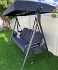 Outdoor Patio Porch Swing With Stand For Three Cushions And Pillow Included Navy Blue All Weather Steel Frame With Adjustable Tilt Canopy For Backyard Front Porch Lawn Three Seat Chill Swing on grass lawn with white fence