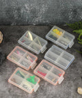 Pack Of 6 Clear Mini Fishing Tackle Boxes With 4 Compartments, containing hooks and lures, on a stone surface outdoors.