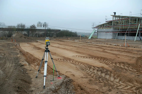 Outdoor construction site with a Beast Dual-Slope Grade Laser Level Kit With HL760 Meter, tripod setup on rough terrain.