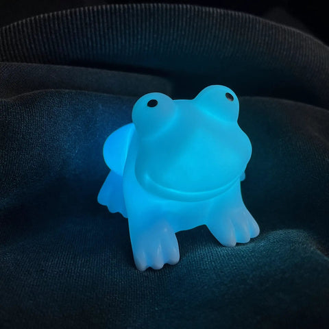Ultra Cute Frog LED Night Light For Kids Room With Automatic Color Changing LEDs glowing blue on dark fabric.