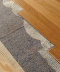 Pro Grade Flooring Underlayment Roll For Laminate Wood And Tile Sound Dampening Padding Compression Resistant Mat For Floating Glue Down Install covers a subfloor with adhesive and wood planks.