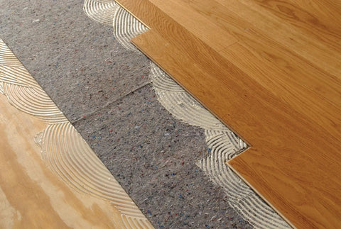 Pro Grade Flooring Underlayment Roll For Laminate Wood And Tile Sound Dampening Padding Compression Resistant Mat For Floating Glue Down Install covers a subfloor with adhesive and wood planks.