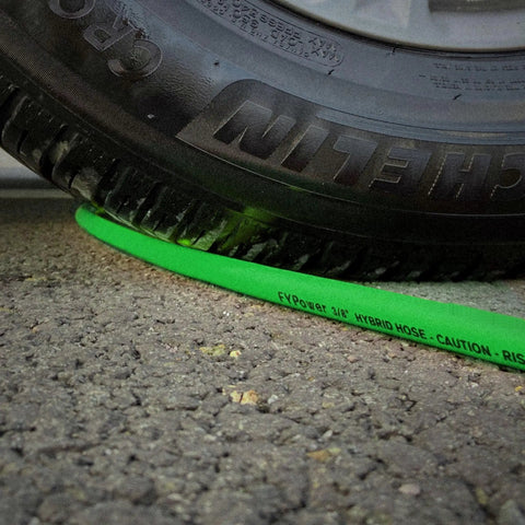Top Shelf Hybrid Air Compressor Hose 3/8 Inch X 25 Feet Kink Free under a tire on asphalt, showcasing durability.