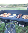 Deluxe Double Burner Steel Griddle With Extra Large 14 Inch By 32 Inch Surface Even Heat Diffusion From Built In Diffuser Plates Pre Seasoned Steel Finish For Easy Outdoor Camping And Backyard Cooking set up outdoors with food cooking on it