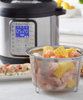 Round Stainless Steel Mesh Steamer Basket For Pressure Cookers filled with corn and shrimp next to an Instant Pot