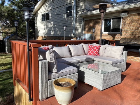 Outdoor deck with wicker furniture, red railing, and solar lights in a residential backyard setting.