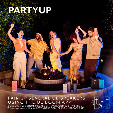 Group of four people dancing around a fire pit with multiple colored UE speakers nearby, using UE Boom app for pairing.