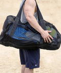 Person carrying XL Mesh Dive Duffel Bag For Scuba And Snorkeling Gear Heavy Duty Travel Duffle with fins and snorkel gear inside