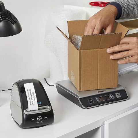 Turbo Driven Direct Thermal Label Printer With Automatic Size Detection And Plug And Play Usb Hookup Plus Lan Networking For Offices Or Shipping Without Any Ink Or Toner Hassle Just A Smooth Operator Ready To Roll Out The Daily Grind next to a cardboard box being filled.