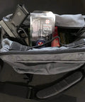 Open tactical bag displaying a handgun, Mil Spec Gun Grease, and ammunition inside compartments, shot from above