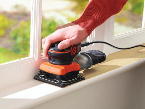 Quarter Sheet Orbital Palm Sander Professional Grade 220 Watt Motor Featuring A Snappy Pressure Trigger Switch Lightweight Orange Body in use on window frame.