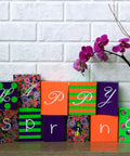 Colorful blocks spelling 'Happy Spring' with purple orchid against white brick wall