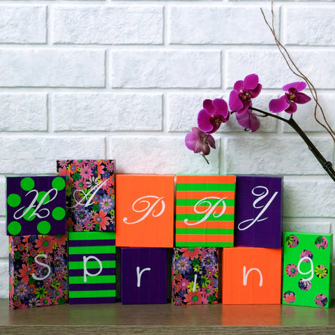 Colorful blocks spelling 'Happy Spring' with purple orchid against white brick wall