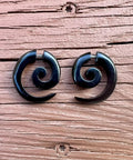 Spiral Fake Gauge Earrings Set In Black With Organic Wood And 316L Surgical Steel displayed on wooden surface