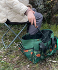 Person sitting on a Foldable Gardening Stool With Detachable Storage Tote For Gardening Camping And Fishing Tools Organizer Portable Garden Chair For Adults With Sturdy Steel Frame And Easy Grab And Go Carry Design