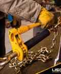 QuikBinder Plus Ratchet Load Binder For Grade 70 And Grade 80 Chain Five Sixteenths To Three Eighths Inch With Folding Handle And 7100 Lbs Working Load Limit Heavy Duty Chain Binder For Secure Trailers Equipment And Towing in use securing chain on trailer with yellow handle.