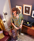 DJ wearing headphones next to receiver with DM 50D BT 5 Inch Desktop Monitor System With Bluetooth For DJs And Beat Makers Dual 2 Way Sound Modes DSP Optimized For DJing Or Production Easy RCA And Mini Jack Connectivity on table