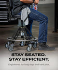 Man seated on Elevated Steel EZ-Lift Shop Chair With Backrest For High Workbenches, 400 Lb Capacity, showing industrial casters in workshop.