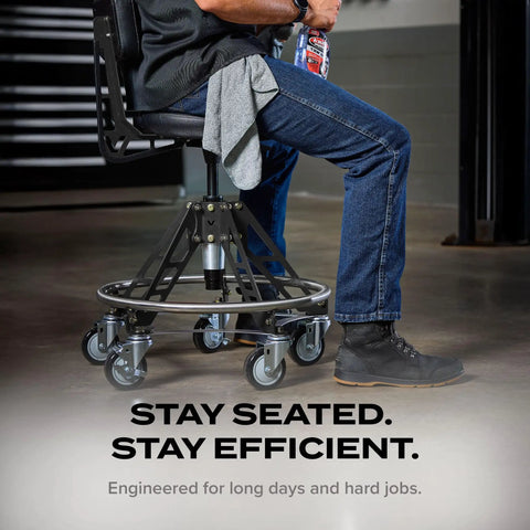 Man seated on Elevated Steel EZ-Lift Shop Chair With Backrest For High Workbenches, 400 Lb Capacity, showing industrial casters in workshop.
