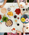 Top view of a colorful brunch table with fruit, pastries, and beverages, featuring donuts being offered on a blue plate.